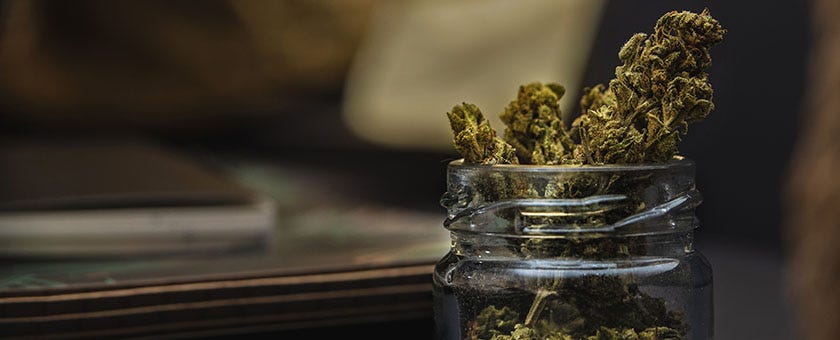 A cannabis flower bud sticking out the top of a small glass jar