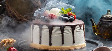 Ice cream cake with fruit on top surrounded by smoke