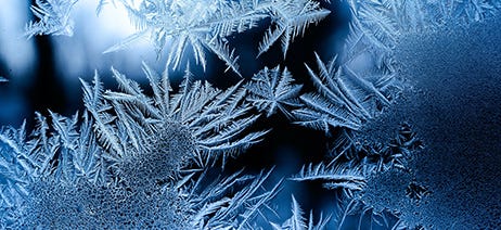 Dark blue frost crystals blossoming across a clear window