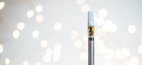 Cannabis vape cartridge in front of a white background with spots of light