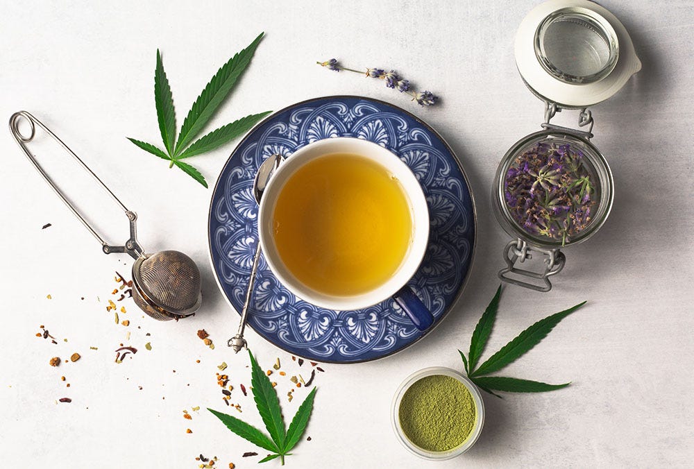 Cup of cannabis tea in a mug surrounded by cannabis leaves, cannabis flower, and kief