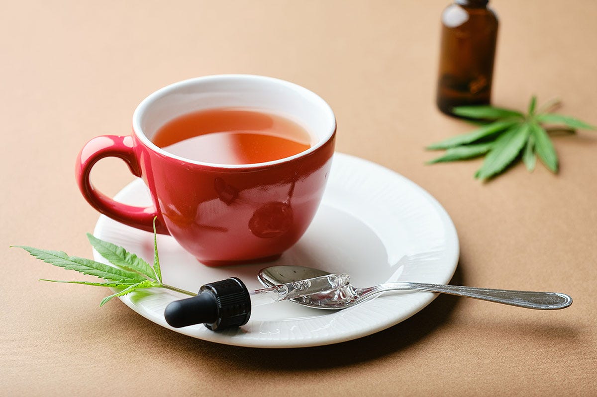 Cup of cannabis tea in a red coffee cup next to a marijuana leaf and an eye dropper