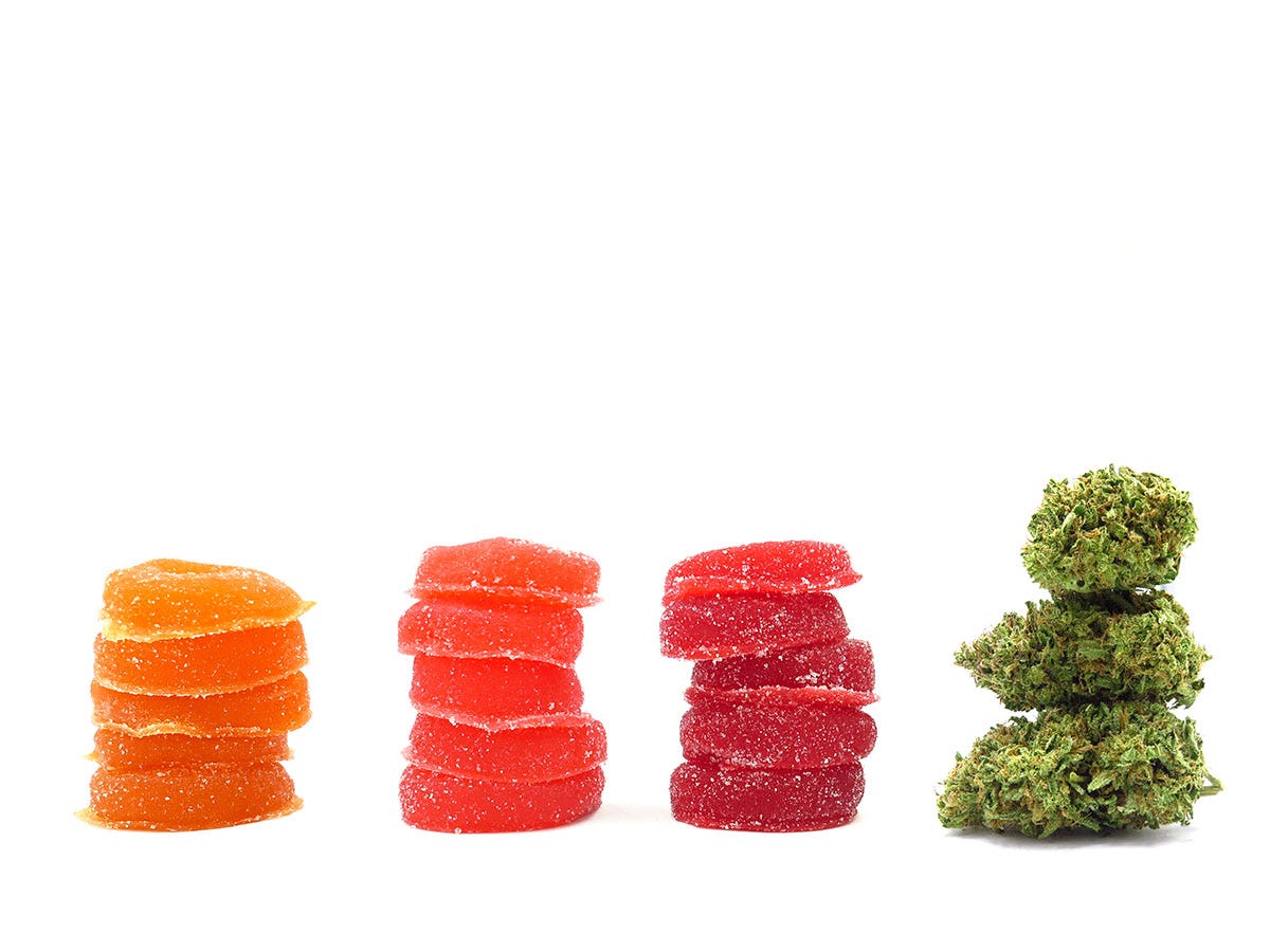 Three stacks of colorful THC gummies next to a cannabis flower bud